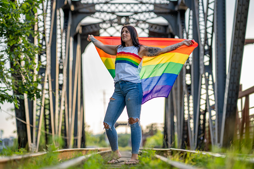 An adult holds a rainbow gay pride flag in the air while standing on a reclaimed rain track.