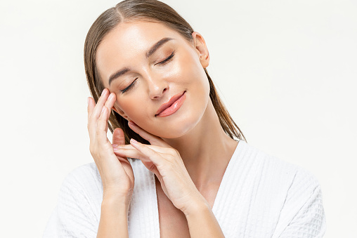 Young beautiful caucasian woman closing her eyes feeling relaxed with hands touching face on isolated white studio background