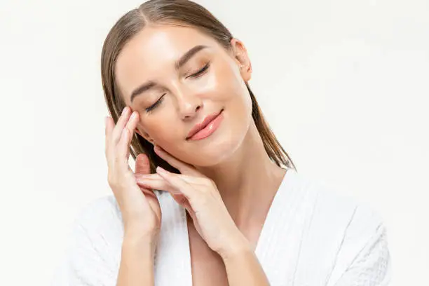Photo of Young beautiful caucasian woman closing her eyes feeling relaxed with hands touching face on isolated white studio background
