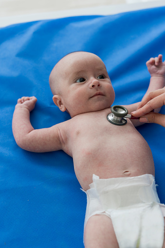 Baby boy 4 to 6 months old, lying on the exam table without a shirt looking at the doctor while they check him