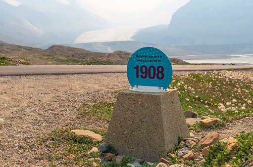 Athabasca glacier with mile post sign showing climate change effect on ice retreat since 1908, with wildfires smoke haze in the air, Alberta, Canada.