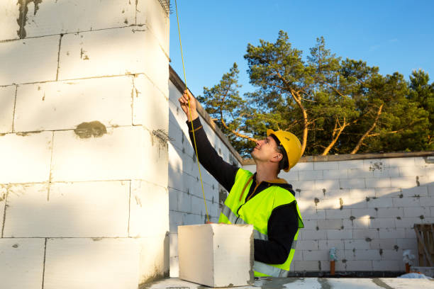 istock Construction worker at construction site measures the length of the window opening and the wall with tape measure. Cottage are made of porous concrete blocks, protective clothing - hardhat and a vest 1332793714