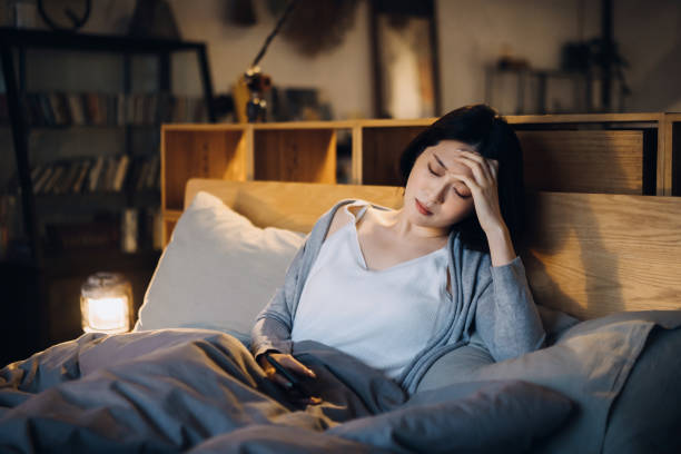 young asian woman feeling sick and suffering from a headache, lying on the bed and taking a rest at home - anemia imagens e fotografias de stock