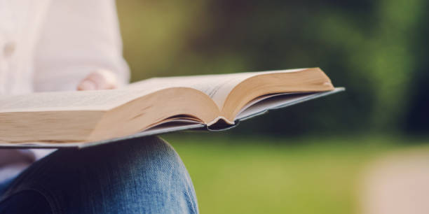istock Lady in white denim jacket reads book turning pages. 1332809652