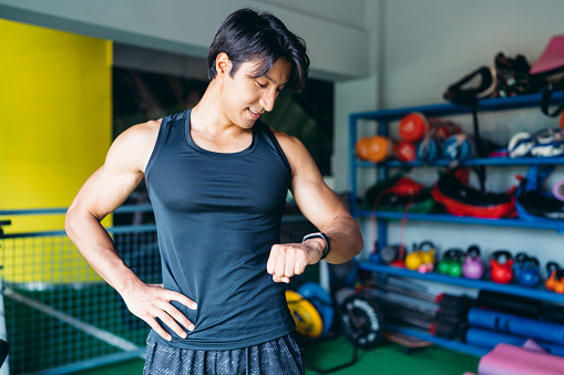 Young muscular sportsman Man checking data on fitness tracker after training in gym.