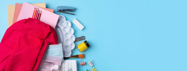 istock Pink backpack with stationery over blue table background. 1332818513