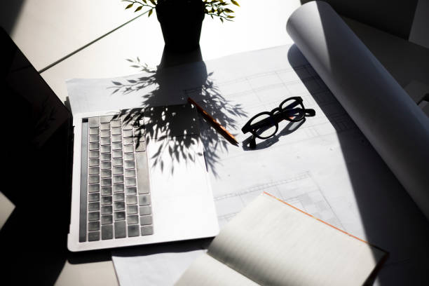 istock High angle view of a workplace Desk with a laptop in office, a notebook and architectural blueprint on the table 1332824747