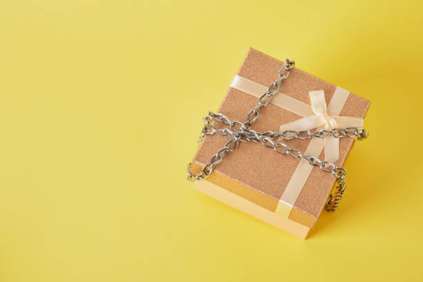 istock shiny pink square gift box tied with chain on yellow background 1332829520