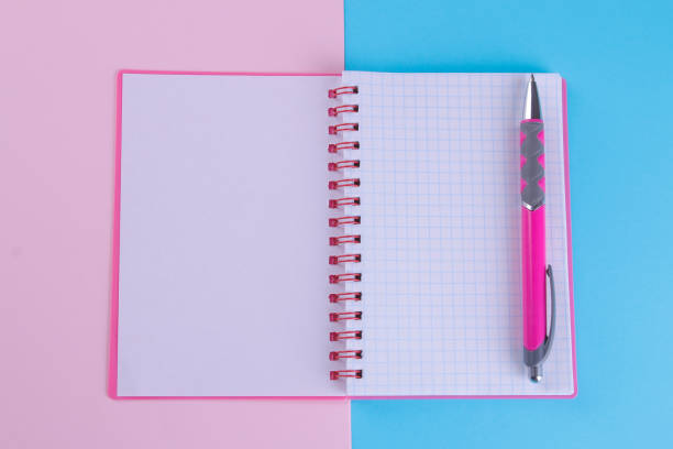 istock Pink notebook in unfolded form with a pink handle on a bright multi-colored background. School supplies 1332835582