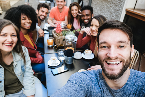 Multiracial friends doing selfie while eating and drinking coffee at vintage bar outdoor - Focus on right man face