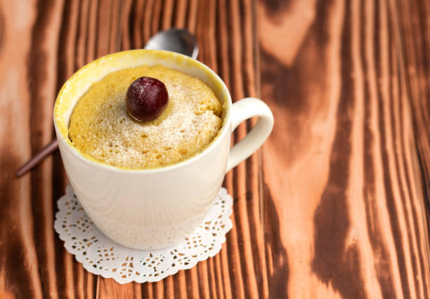 muffin dans une tasse, cuit au micro-ondes. dessert à la vanille avec cerise sur le dessus - over easy photos et images de collection