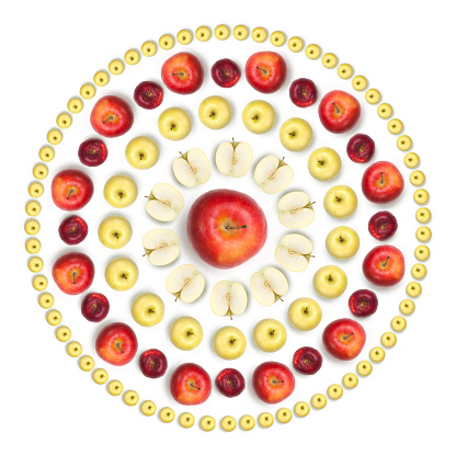 Composition made with various kinds of healthy apples, arranged into a wheel shaped like a sun, showing whole fruits and slices. White background.