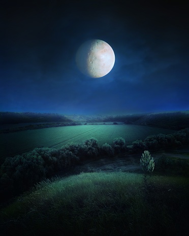Big moon in the night sky over green hills and valleys. Bright light from the full moon. Beautiful night landscape.