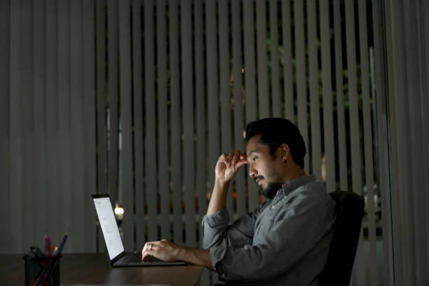 istock Tired man with computer working late at night at the office at night 1332844429