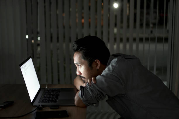 istock Tired man with computer working late at night at the office at night 1332844512