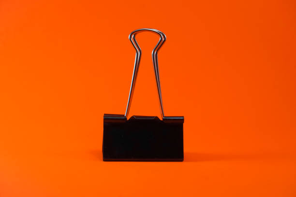 Binder clip is black on an orange background. Black iron paperclip