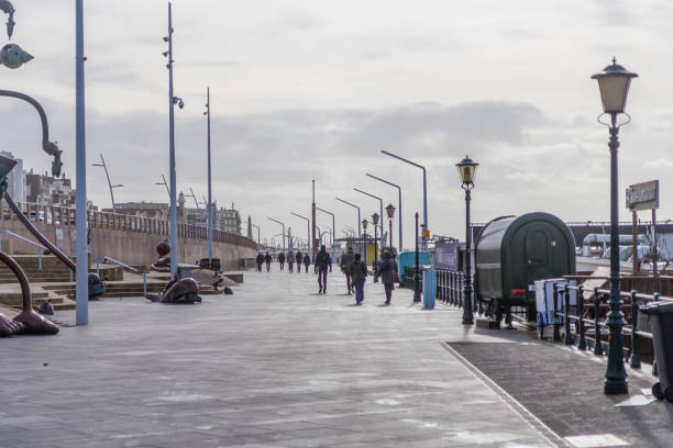 Scheveningen, the Netherlands - Mar 12, 2021: The boulevard of Scheveningen with some people walking in windy weather during lockdown