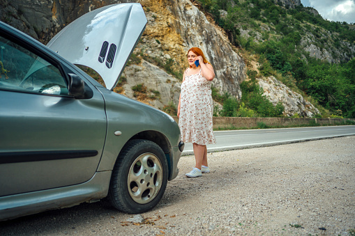 Young overweight woman calling a car assistance service with her smartphone, her car has broken down