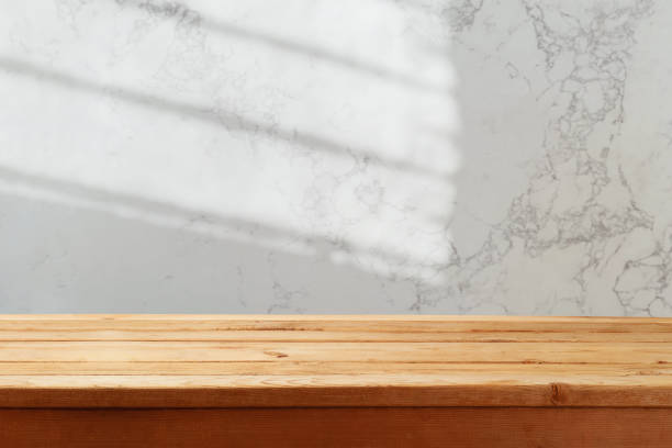 istock Empty wooden table over marble wall and light rays from window background. Kitchen counter top for mock up design 1332852080