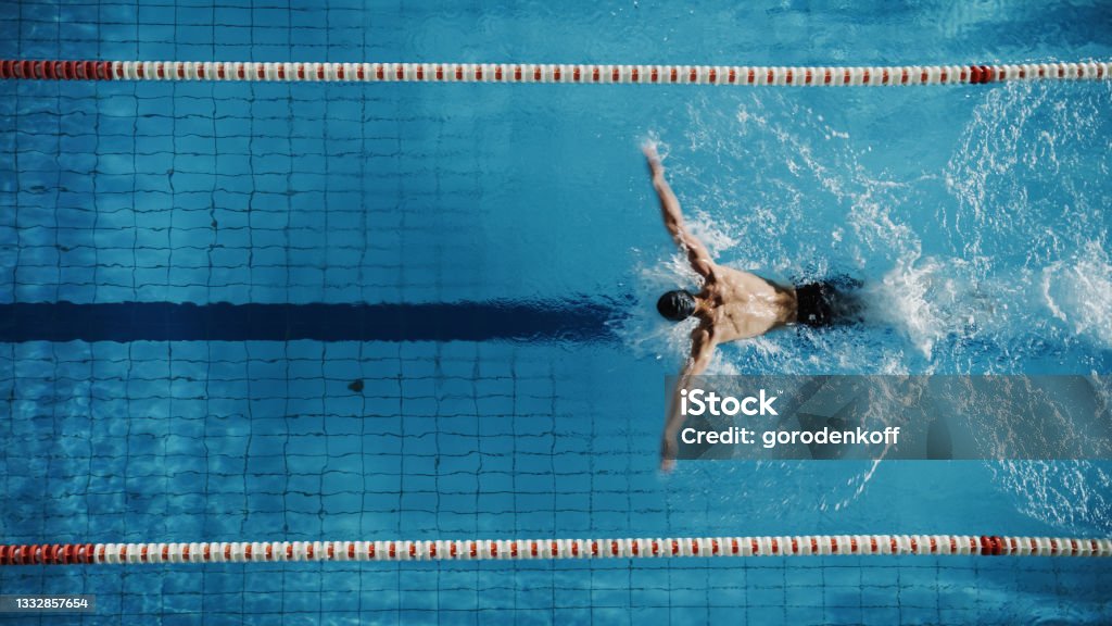 Aerial Top View Male Swimmer Swimming in Swimming Pool. Professional Determined Athlete Training for the Championship, using Butterfly Technique. Top View Shot Swimming Stock Photo