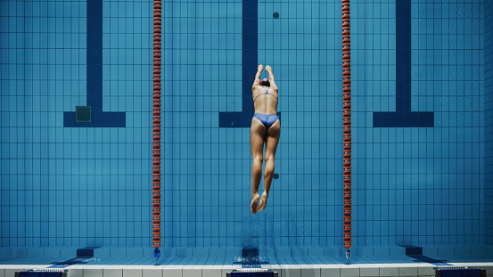 Beautiful Female Swimmer Diving in Swimming Pool. Professional Athlete Jumps into Water. Person Determined to Win Championship. Stylish Colors, Top Down Shot.