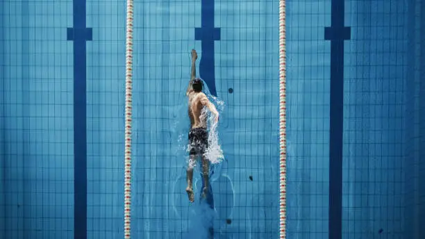 Photo of Aerial Top View Male Swimmer Swimming in Swimming Pool. Professional Athlete Training for the Championship, using Front Crawl, Freestyle Technique. Top View Shot