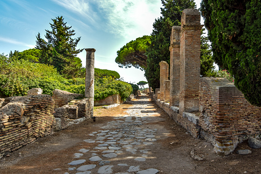 Ancient roman road and ruins with trees and cloudy sky in Ostia Antica