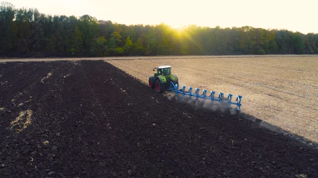 The tractor is plowing the field from the top. The tractor works in the field in the evening. View from the drone. Modern tractor plows the field
