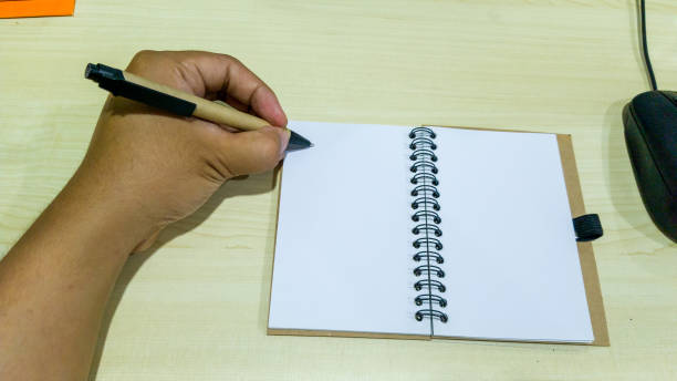 istock southeast asian man left hand writing on blank note near mouse on wooden table 1332865127