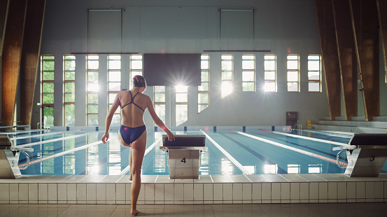 Athletic Young Female Swimmer Comes to Starting Block and Prepairing to Jump into Swimming Pool. Healthy Professional Woman Athlete Training for the Championship. Wide Shot