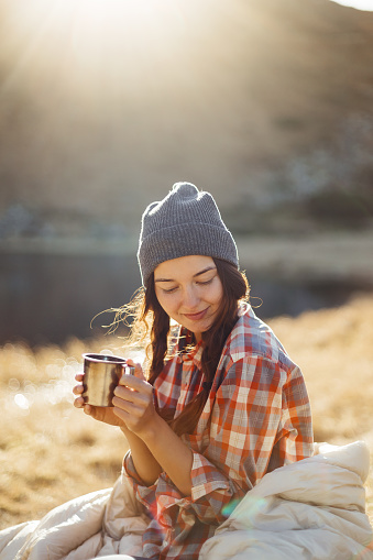 Portrait of beautiful traveler woman hiking in the mountains with a cup of drink near lake, camping travel concept. Girl on vacation enjoying the beauty of nature.