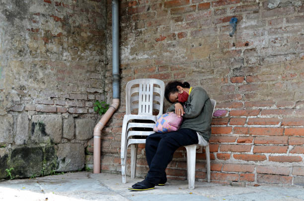 mujer sin hogar durmiendo en una silla monobloque al lado de la pared de ladrillo en un antiguo cementerio. - brick wall homelessness wall begging fotografías e imágenes de stock
