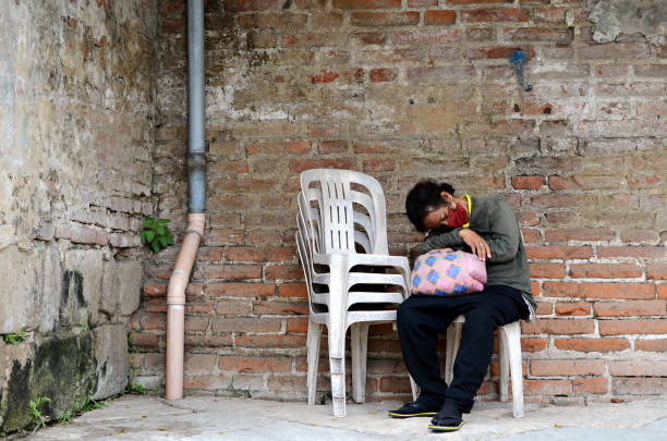 mujer sin hogar durmiendo en una silla monobloque al lado de la pared de ladrillo en un antiguo cementerio. - brick wall homelessness wall begging fotografías e imágenes de stock