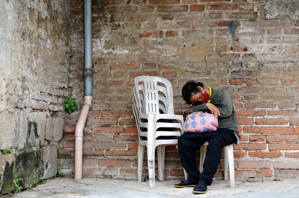 femme sans abri dormant sur une chaise monobloc sur le côté du mur de briques dans un vieux cimetière. - brick wall homelessness wall begging photos et images de collection