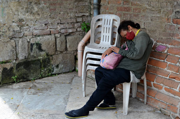 mujer sin hogar durmiendo en una silla monobloque al lado de la pared de ladrillo en un antiguo cementerio. - brick wall homelessness wall begging fotografías e imágenes de stock