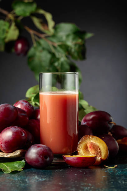 Glass of plum juice on a table with fresh purple plums.