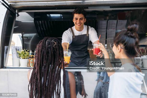 Back View Of Two Females Buying Drinks From A Male Owner At A Food Truck Smiling Entrepreneur Giving Drinks To Clients Stock Photo - Download Image Now