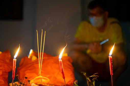 Singapore, Singapore - August 7, 2021: A man watches as candles and joss sticks placed on the ground burn before him.