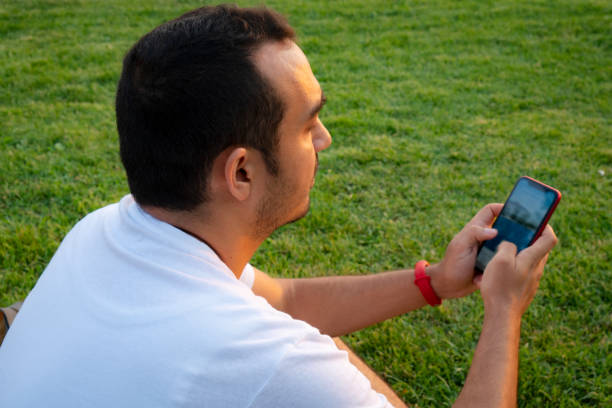 istock Young man sitting on grass and using smart phone. 1332885910