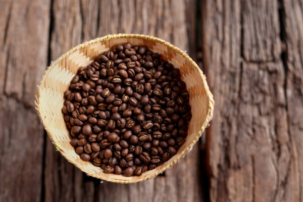 Coffee Beans Peaberry large group of objects small size picking in bamboo basket. log wooden background. Selective focus on foreground with copy space.