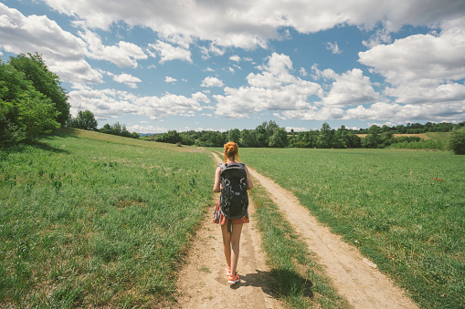 adult female hiker hiking in nature on beautiful summer day with cumulus clouds in the sky