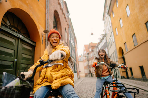 Photo of two young women riding bikes and having fun while discovering the new city together.