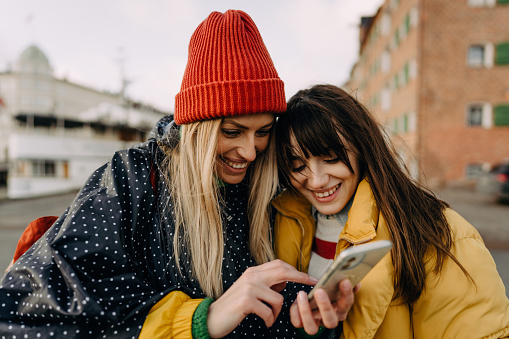 Photo of two young women looking for a place on the map as exploring the city; sisters traveling together and having fun while getting to know the new city.