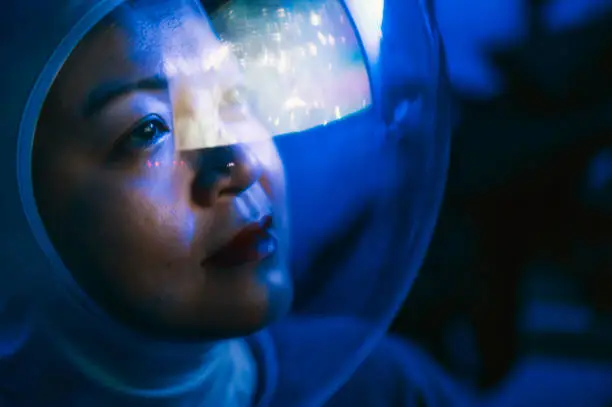 Photo of Asian chinese mid adult female astronaut looking at earth through window from spaceship at outer space