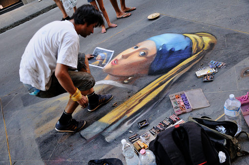 Florence, Italy - August 19, 2011: A street painter draws a picture Girl with a pearl earring on the street of Florence on the asphalt with colored crayons.