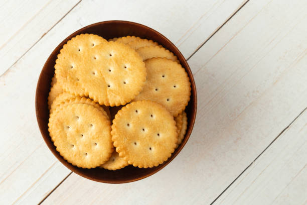 istock Rounded cracker cookies in a wooden bowl on white wooden table background 1332900268