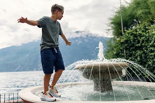 Family enjoying vacations in Limone sul Garda, Italy. Teenage boy is walking at the edge of the fountain. Cool overcast day.\nCanon R5