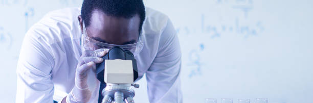 African male scientist looking in microscope in laboratory, Testing for research about Covid-19 vaccine stock photo