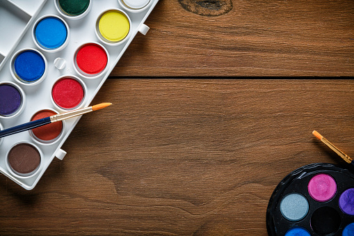 Back to school themes. Close-up of watercolor paint sets and paintbrushes on wooden desk