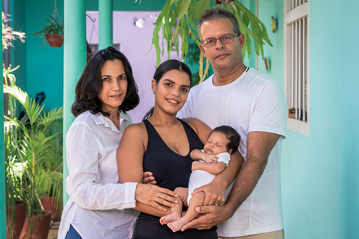 Photo of a group of people standing. Composed of a baby in the arms of a young woman, a man and a woman